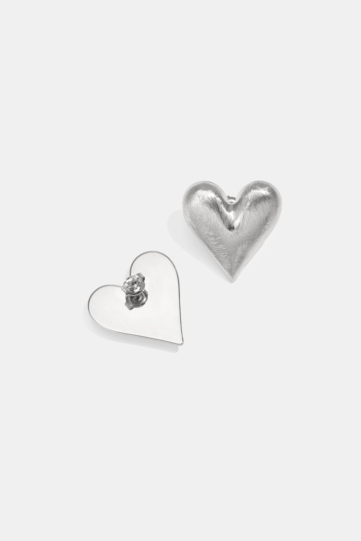 Close-up of silver puffed heart stud earrings with brushed texture on a white background