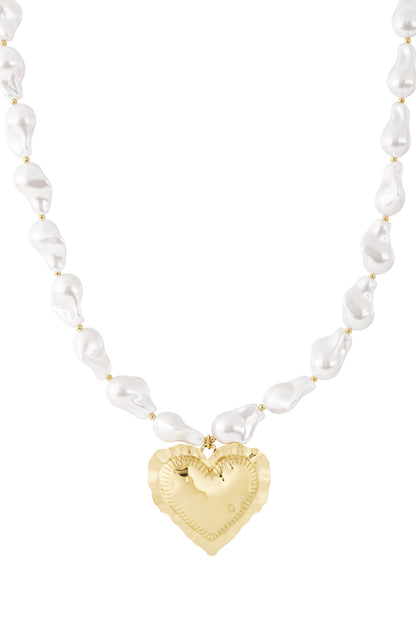 Close-up of a baroque pearl necklace featuring irregular white pearls and a hammered gold heart pendant