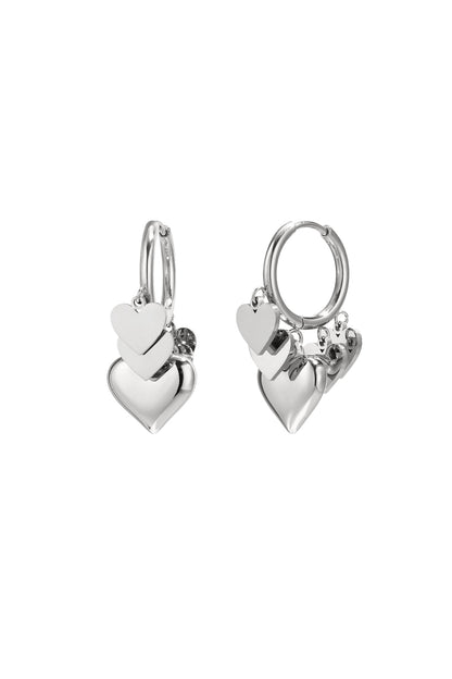 Pair of silver drop earrings with three layered heart charms hanging from hoops on white background