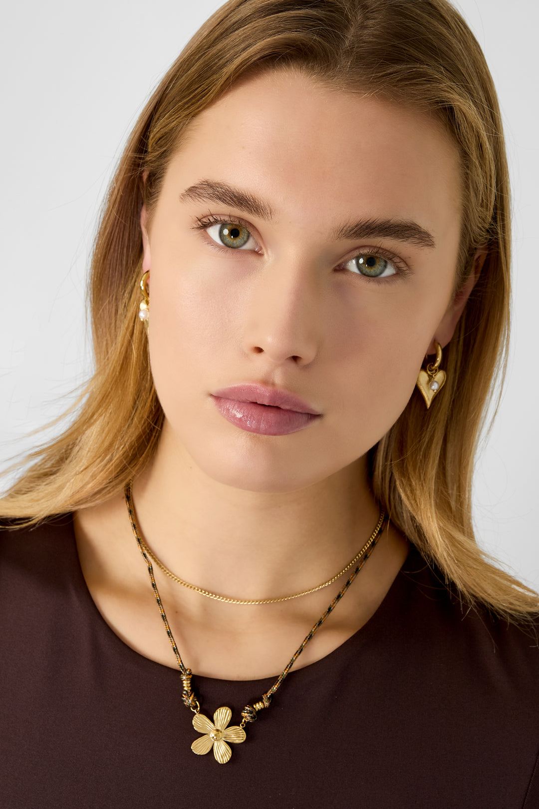 Close-up of woman wearing the gold flower pendant necklace layered with a delicate gold chain and brown top