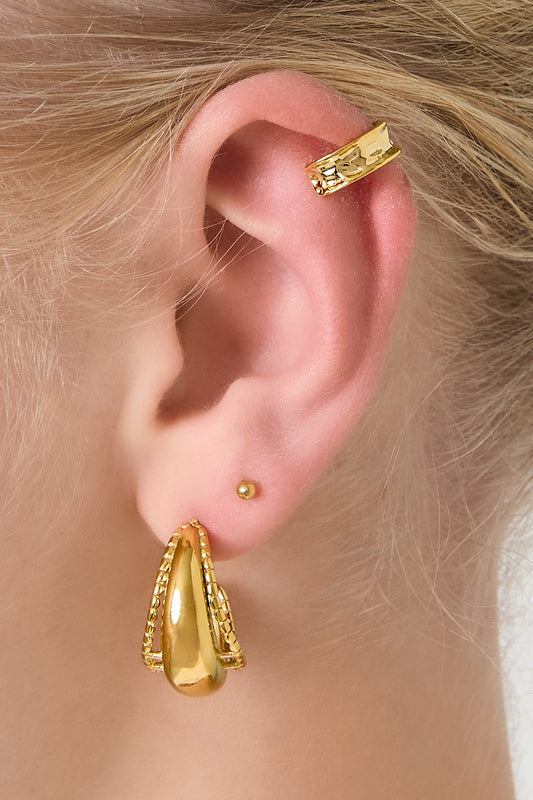 Close-up of a woman's ear wearing a hammered gold ear cuff on the cartilage and layered gold earrings on the lobe