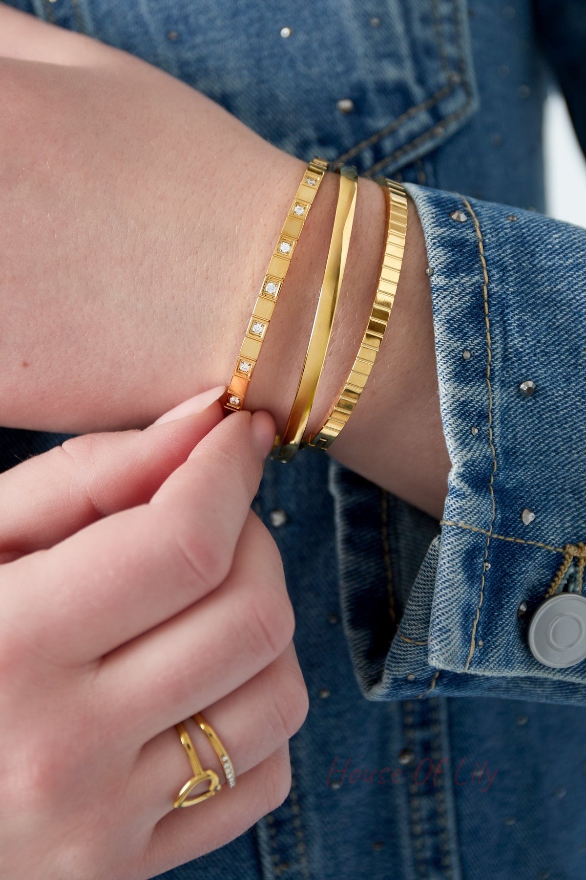 Woman wearing layered gold bracelets with denim jacket and gold rings