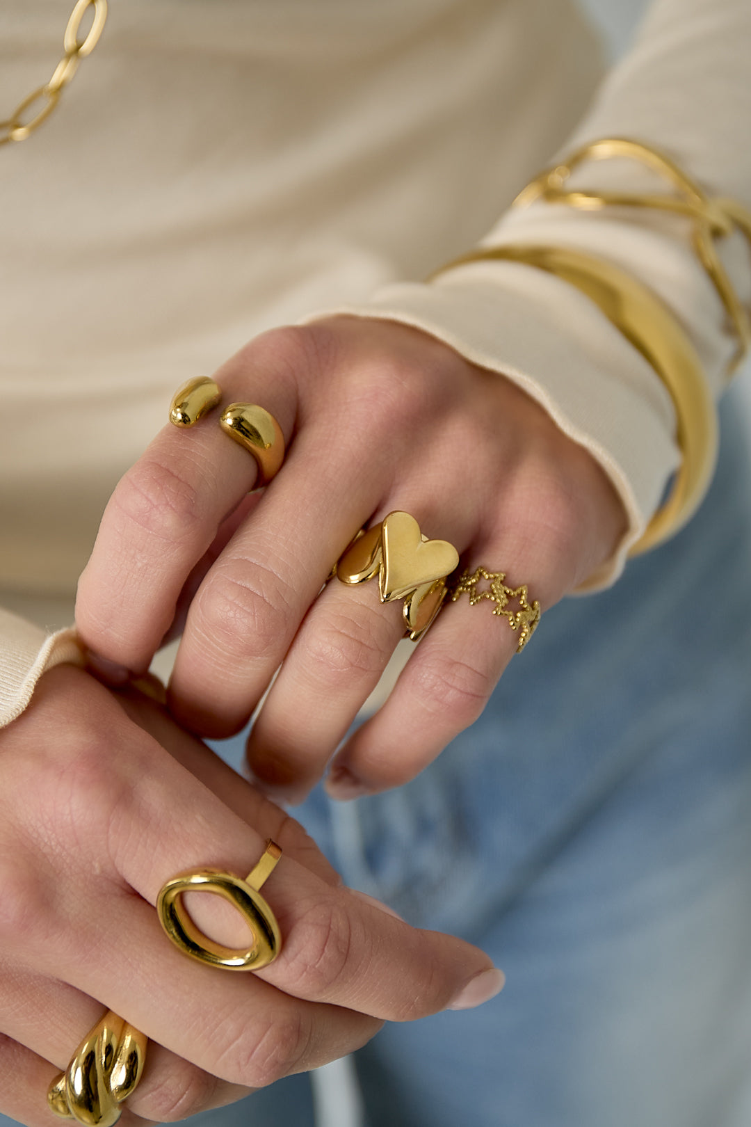 Close-up of female hand wearing gold heart statement ring with other gold rings and bracelets.