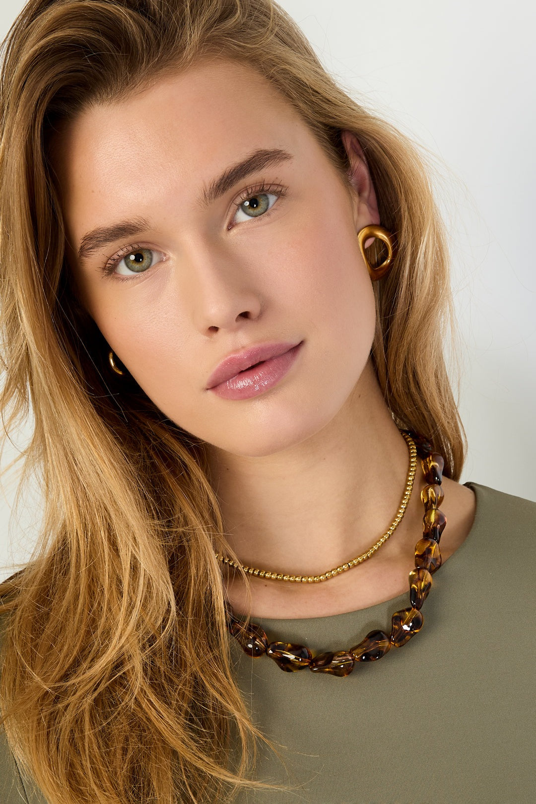 Woman wearing tortoiseshell beaded necklace paired with a gold ball-chain necklace and gold earrings, close-up portrait