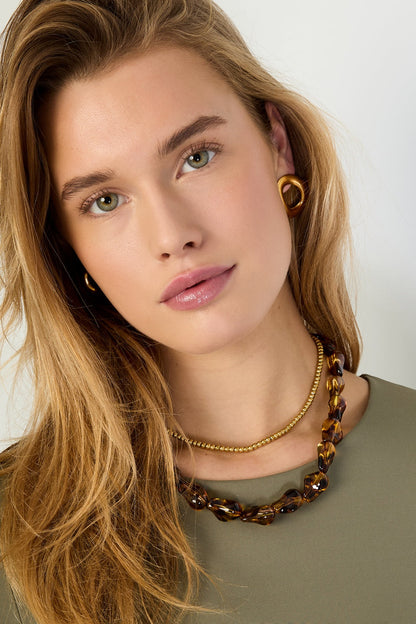 Woman wearing tortoiseshell beaded necklace paired with a gold ball-chain necklace and gold earrings, close-up portrait