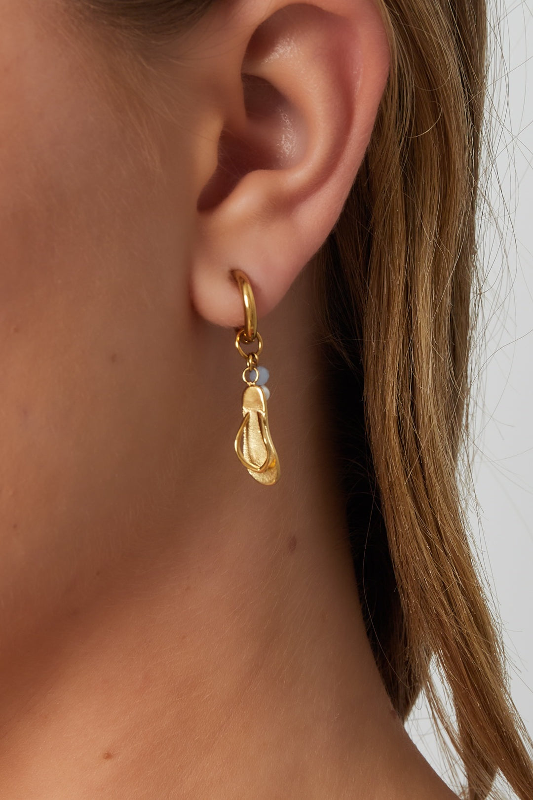 Close-up of a woman wearing one gold flip flop dangle earring showcasing its charm and bead details