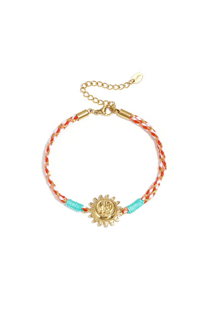 Close-up of light blue braided rope bracelet with gold cowrie shell charm on white background