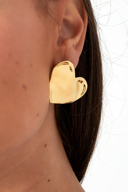 Close-up photo of gold chunky heart stud earring worn on a woman's ear showcasing size and shine