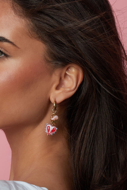 Closeup side profile of model wearing gold hoop earrings with pink heart charm on pink backdrop