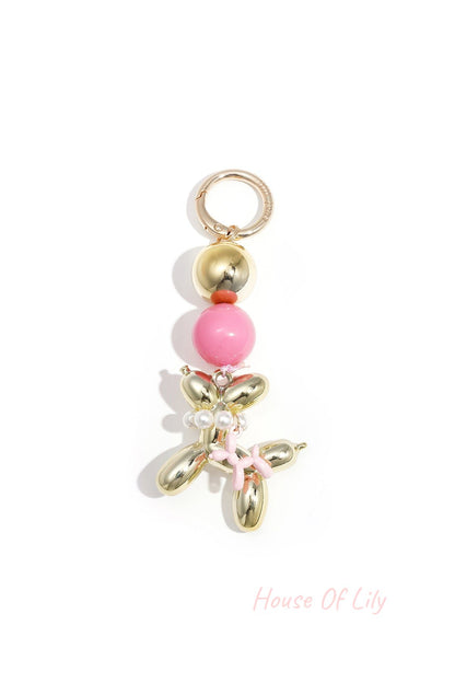 Gold-tone balloon dog keychain with bright pink acrylic bead and pink balloon charm on white background