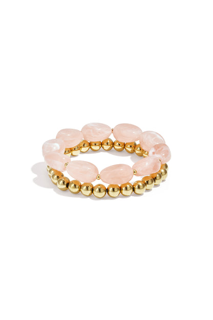 Close-up of two beaded stretch bracelets featuring oval pink resin beads and gold-tone round beads on white background