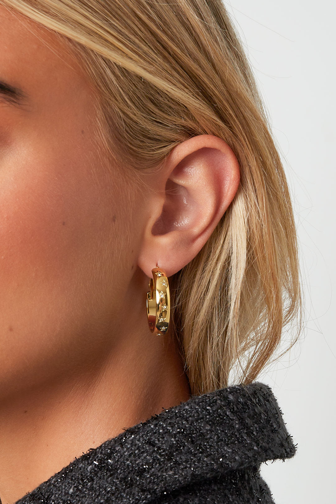 Close-up of woman wearing gold star-embellished hoop earrings showcasing youthful chic style