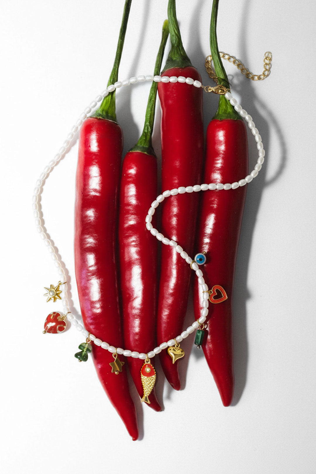 The beaded charm necklace creatively draped over bright red chili peppers showing playful design