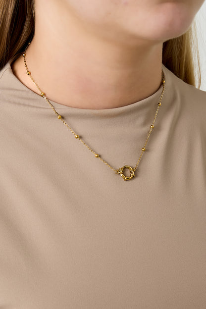 Woman wearing dainty gold chain necklace with small gold beads and circular clasp over beige top