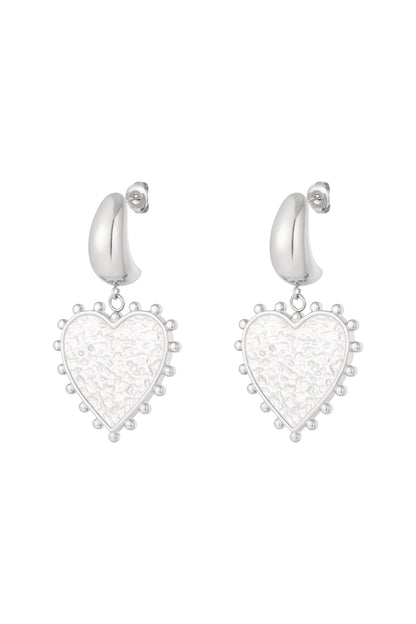Pair of silver modern heart-shaped drop earrings with textured centers and dotted edges on white background