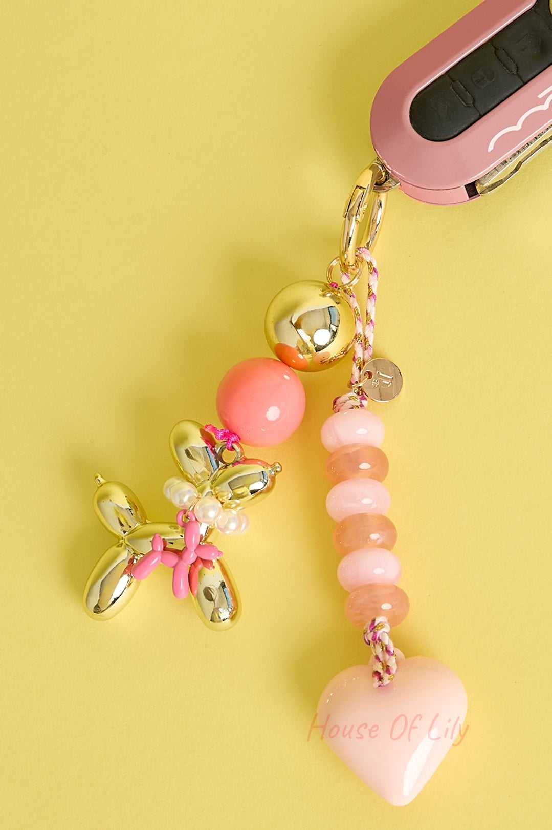 Balloon dog keychain attached to pink car key displaying coral, pink, and heart-shaped bead charms on yellow background