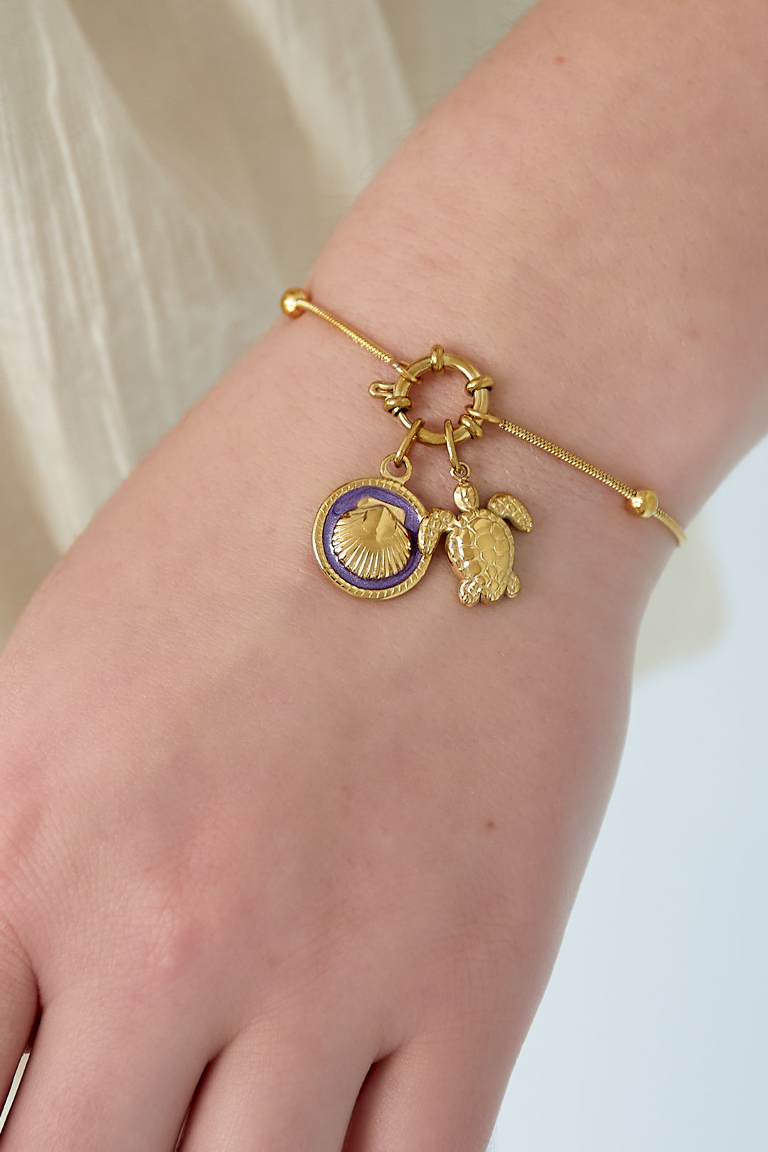 Close-up of gold charm bracelet with turtle and purple-enamel seashell charms worn on wrist