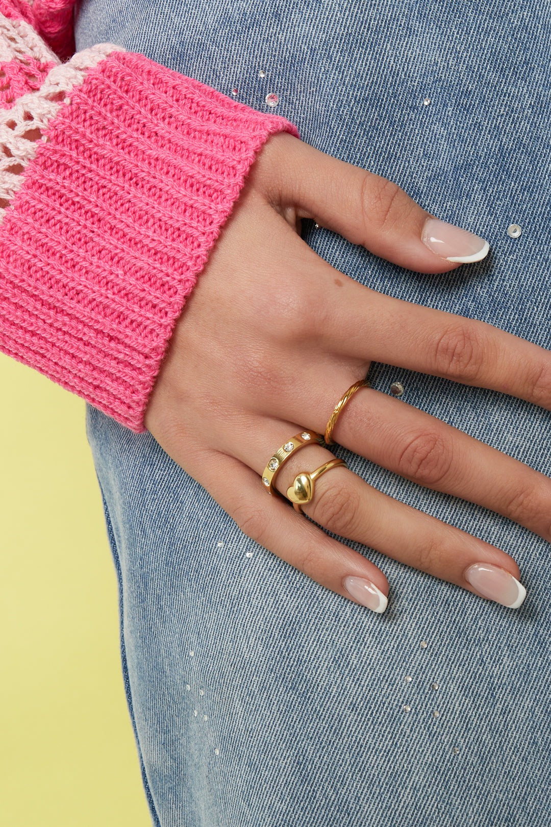 Close-up of hand wearing gold ring with crystal accents, paired with other gold rings and pink knit sweater cuff
