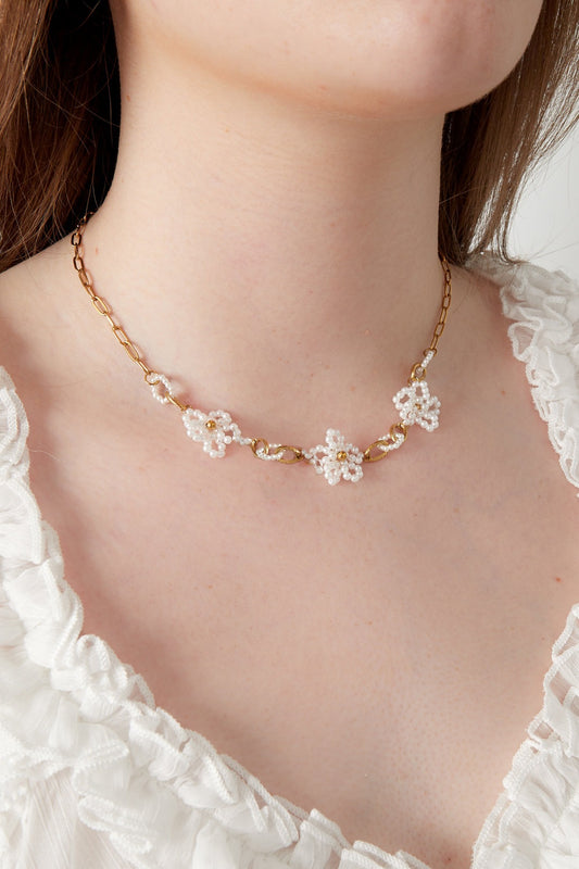 Close-up of a woman wearing a gold-plated chain necklace adorned with delicate white pearl flowers against a white ruffled top