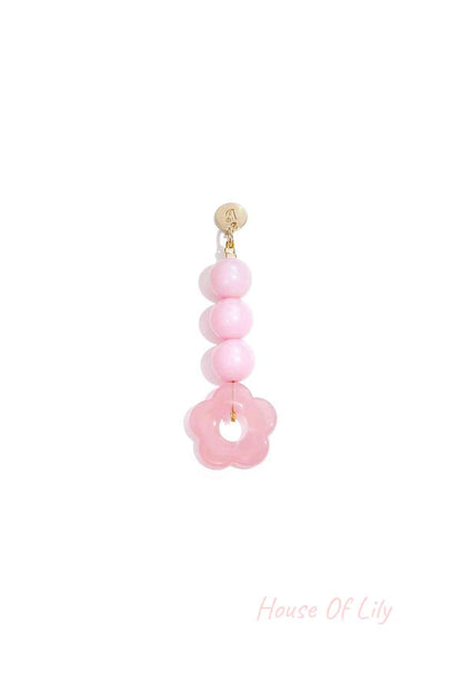 Transparent pink acrylic flower bag charm with three round pink beads hanging from a gold clasp on white background