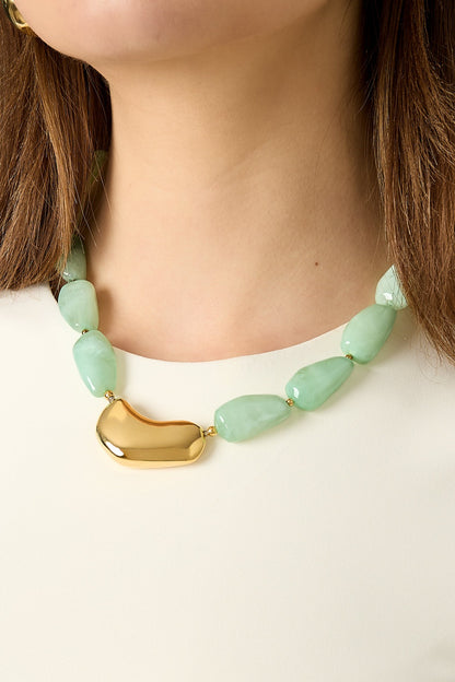 Close-up of model wearing mint green chunky beaded necklace with shiny gold centerpiece against a white top