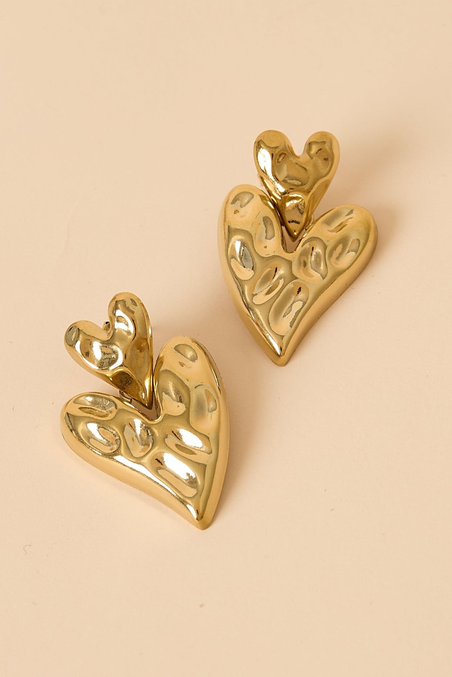 Close-up of gold chunky heart drop earrings with hammered finish on beige background