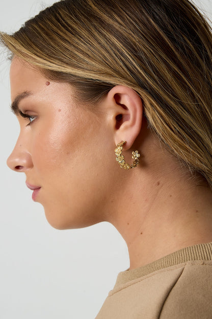Close-up of a woman’s ear wearing one gold floral hoop earring, focusing on the floral design details.