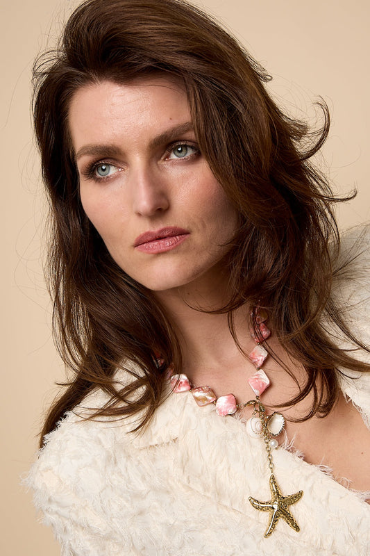 Close-up portrait of woman wearing pink and cream shell bead necklace with starfish charm against beige background