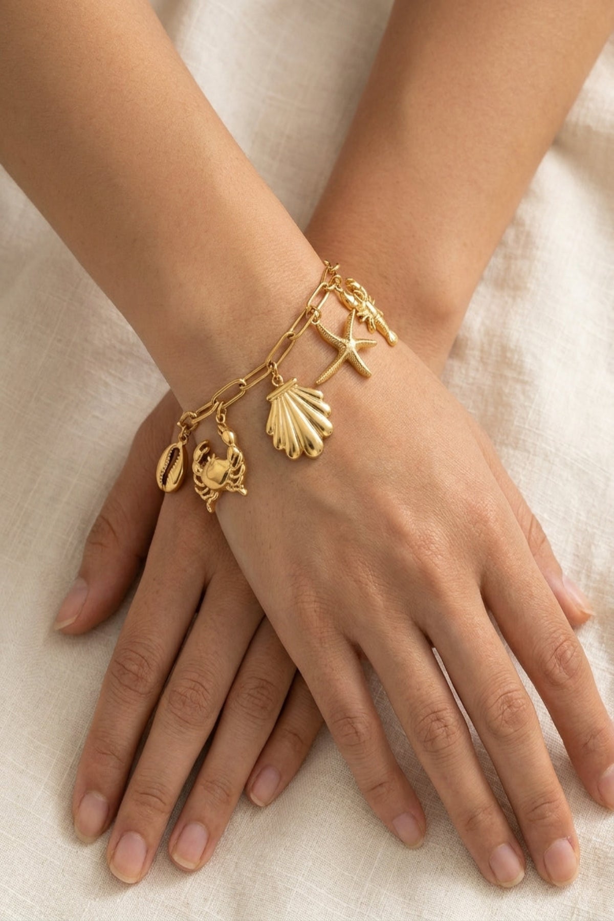 Gold bracelet with charms on a person's wrist against a neutral background