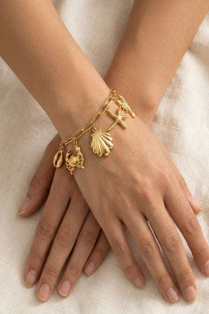 Gold bracelet with charms on a person's wrist against a neutral background
