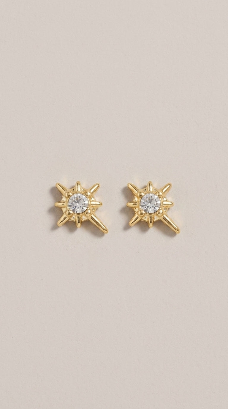Gold stud earrings featuring a central crystal surrounded by a starburst design with one elongated ray.