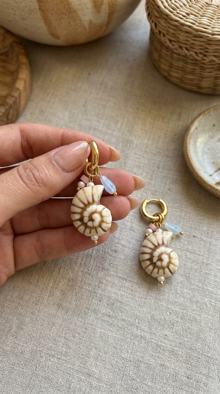 Shell Hoop Drop Era earrings: gold hoops with nautilus shell charms, small pearls, pink beads, and blue opalescent drops.