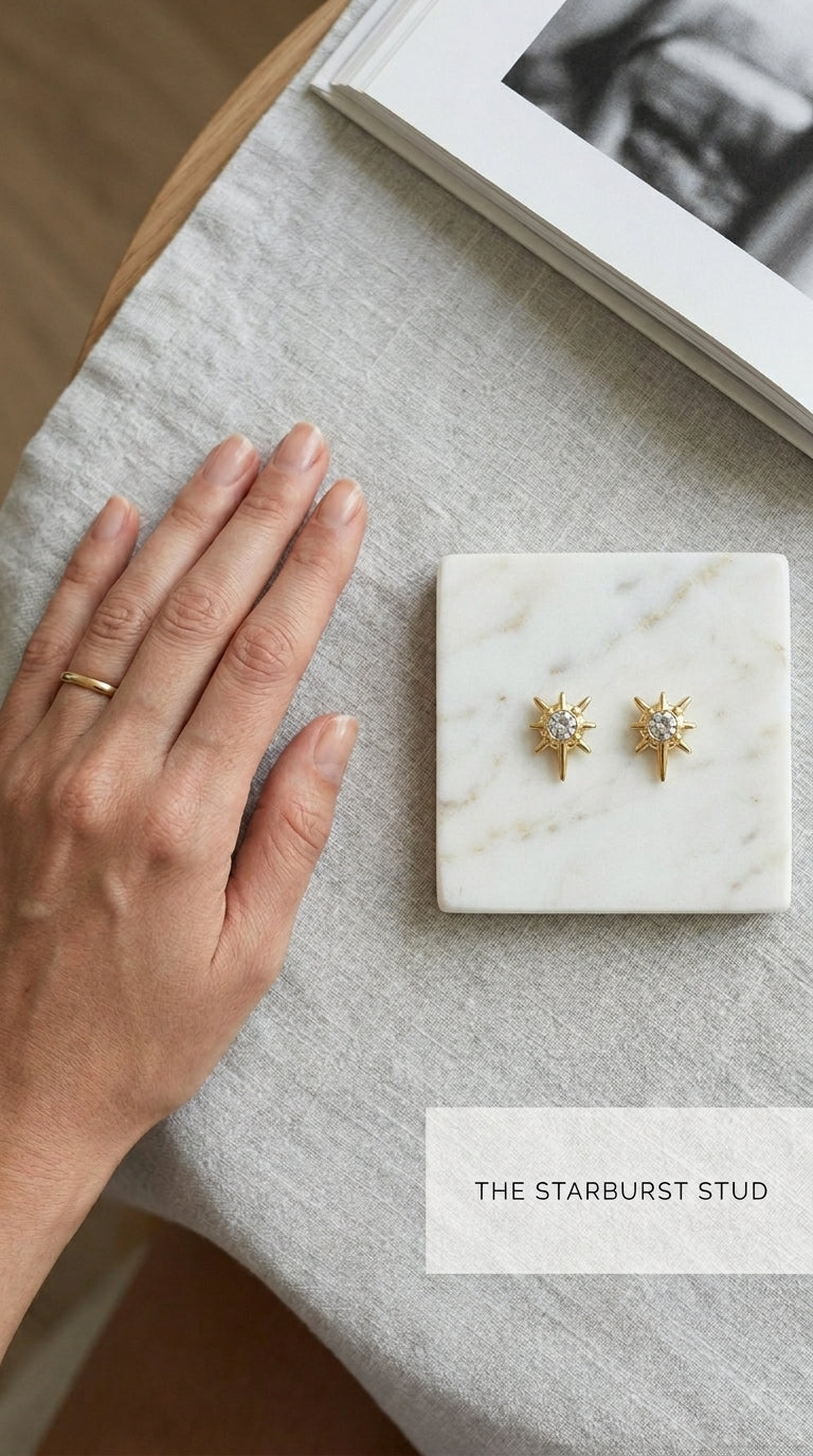 Gold starburst stud earrings featuring central white crystals, displayed on a marble square next to a simple gold ring.