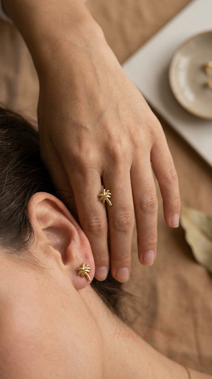 Gold palm tree stud earring and matching ring on a model against a neutral background.