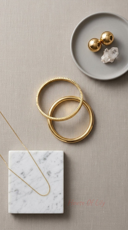 Two gold bangles, one smooth and one textured, paired with a delicate gold chain and gold sphere earrings.