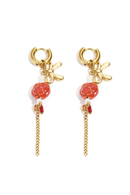 Pair of gold-tone floral drop earrings featuring bow motifs, orange flower beads, faux pearls, and dangling gold chains on white background