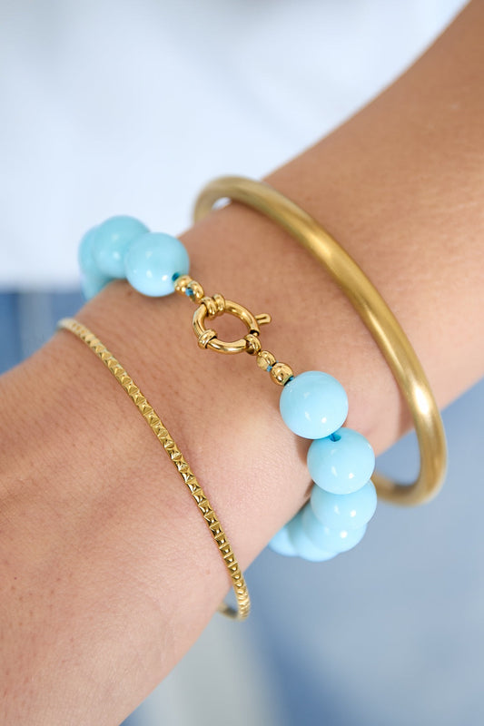 Blue resin bead bracelet with gold toggle clasp styled with gold bangles on wrist