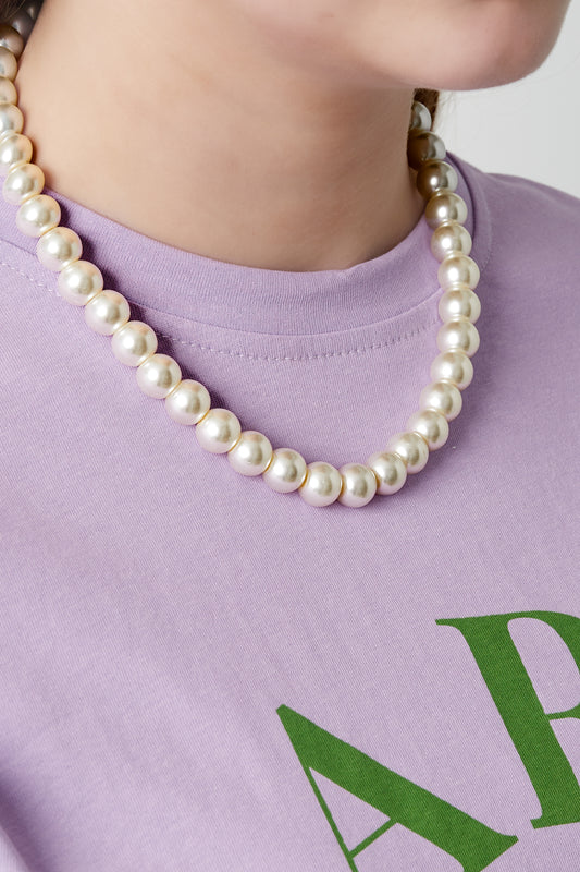 Model wearing a short pearl beaded necklace paired with a light purple shirt featuring green letters