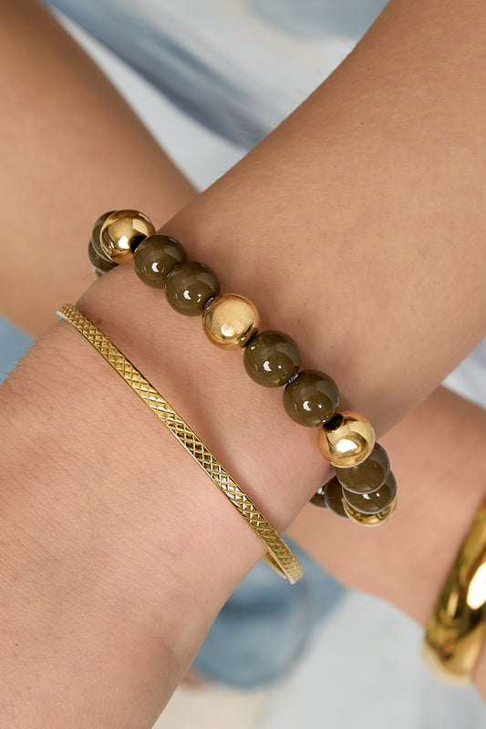 Close-up on wrist wearing brown and gold-tone acrylic beaded bracelet paired with thin gold bangle