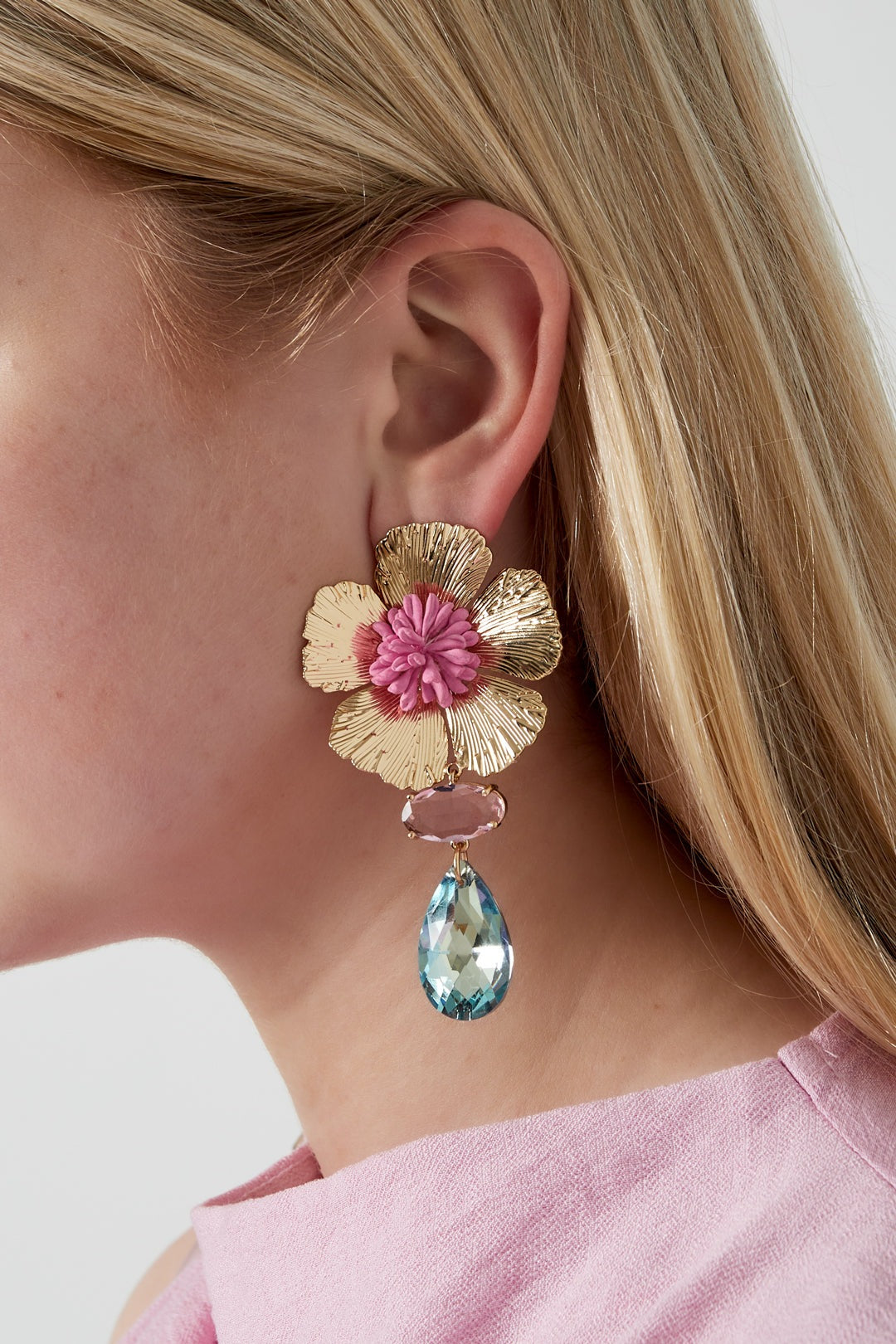 Close-up of woman wearing floral drop earring with pink resin center and light blue faceted crystal, showcasing bold statement design