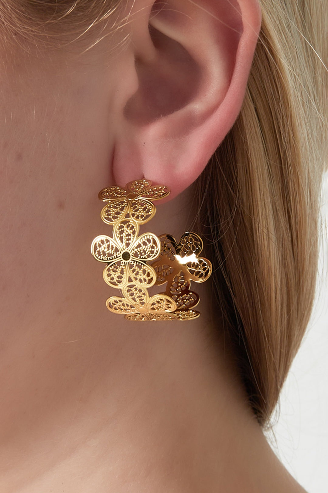 Close-up of a woman wearing gold floral hoop earrings with intricate flower cut-outs