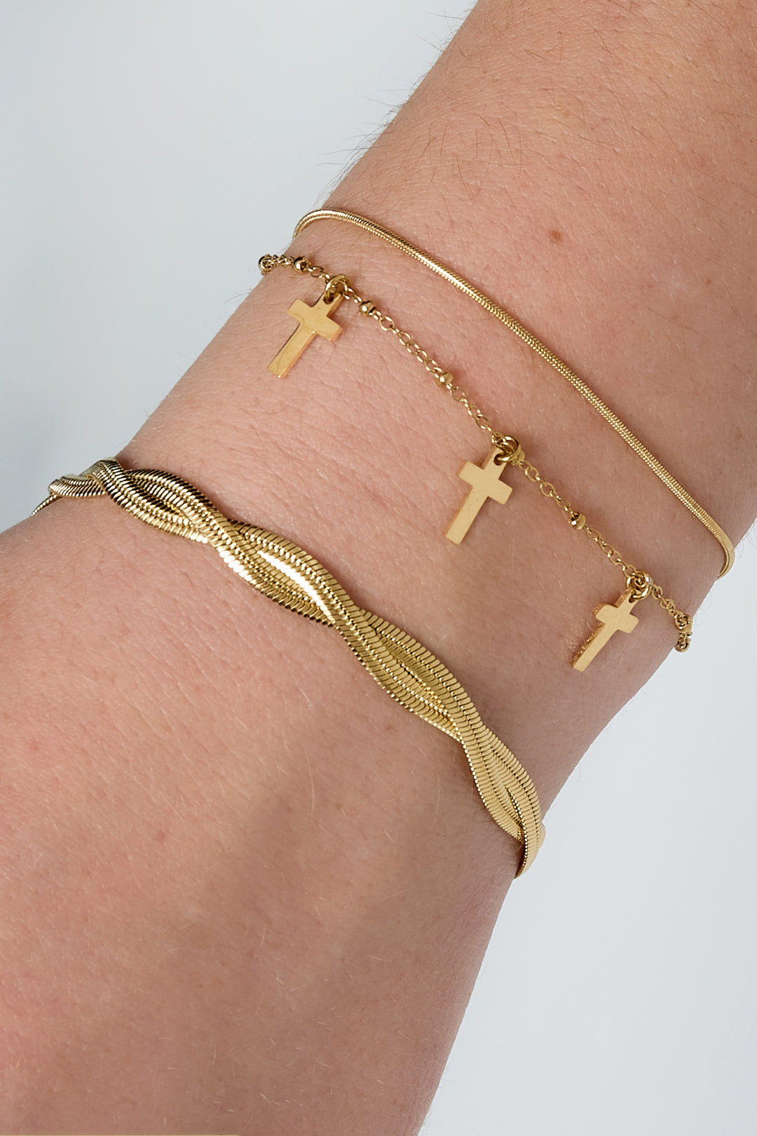 Three gold bracelets stacked on wrist featuring twisted chain, cross charms, and smooth thin chain