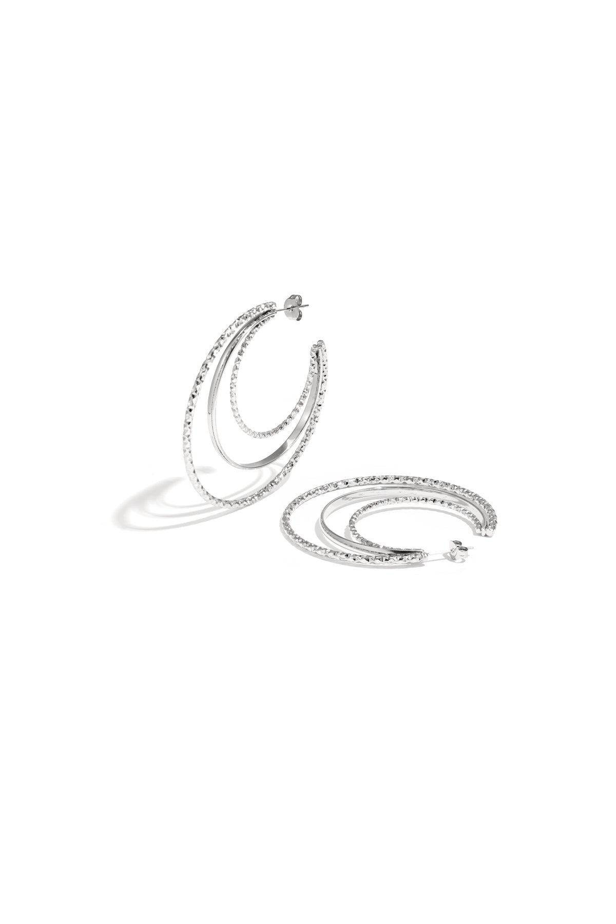 Layered triple hoop earrings in silver featuring two textured hammered hoops and a smooth middle hoop arranged on a white background