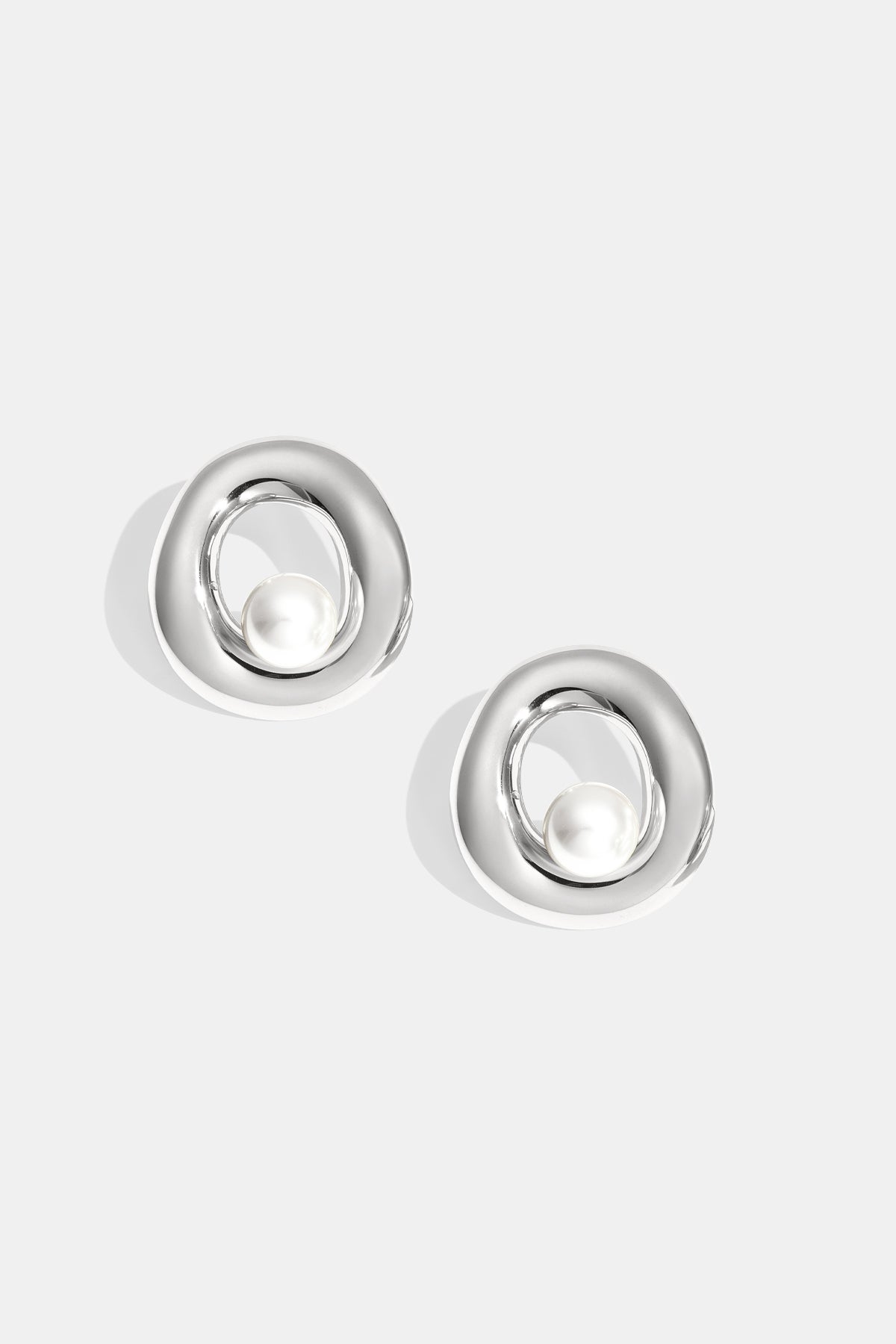 Pair of silver-tone circle stud earrings with pearl centerpiece on white background
