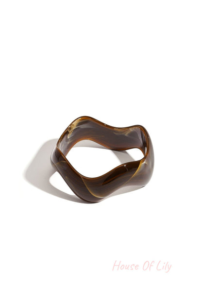 Brown acrylic bangle with marbled swirls and irregular shape cast in shadow on white background