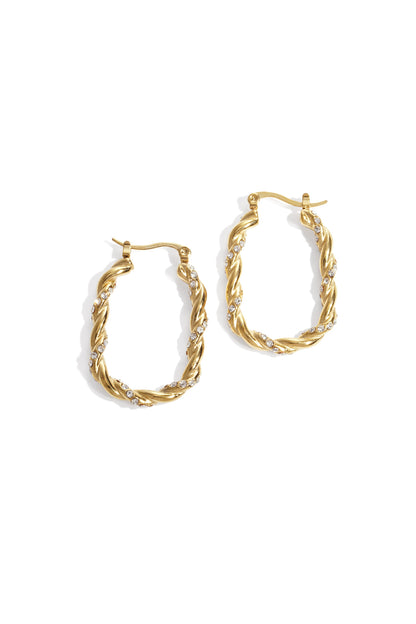 Close-up of gold twisted hoop earrings adorned with rhinestones on white background