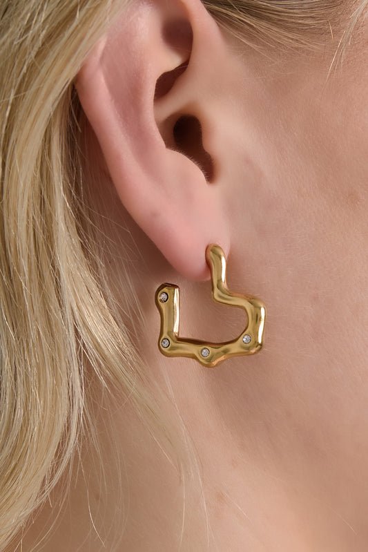 Close-up of a gold wavy hoop earring worn on a woman's ear showcasing the design and rhinestones
