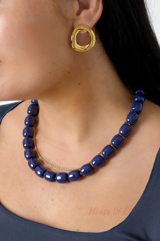 Model wearing glossy navy chunky acrylic bead necklace paired with gold modern irregular shaped stud earrings and blue top
