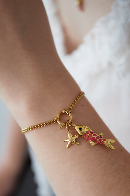 Close-up of the gold plated ocean charm bracelet worn on a woman's wrist showcasing the fish and starfish charms