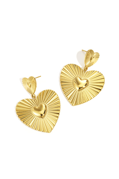 Pair of gold heart-shaped drop earrings with grooved texture and shiny center hearts on white background